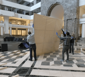 Museum staff lifting a large wrapped artwork in an atrium space.